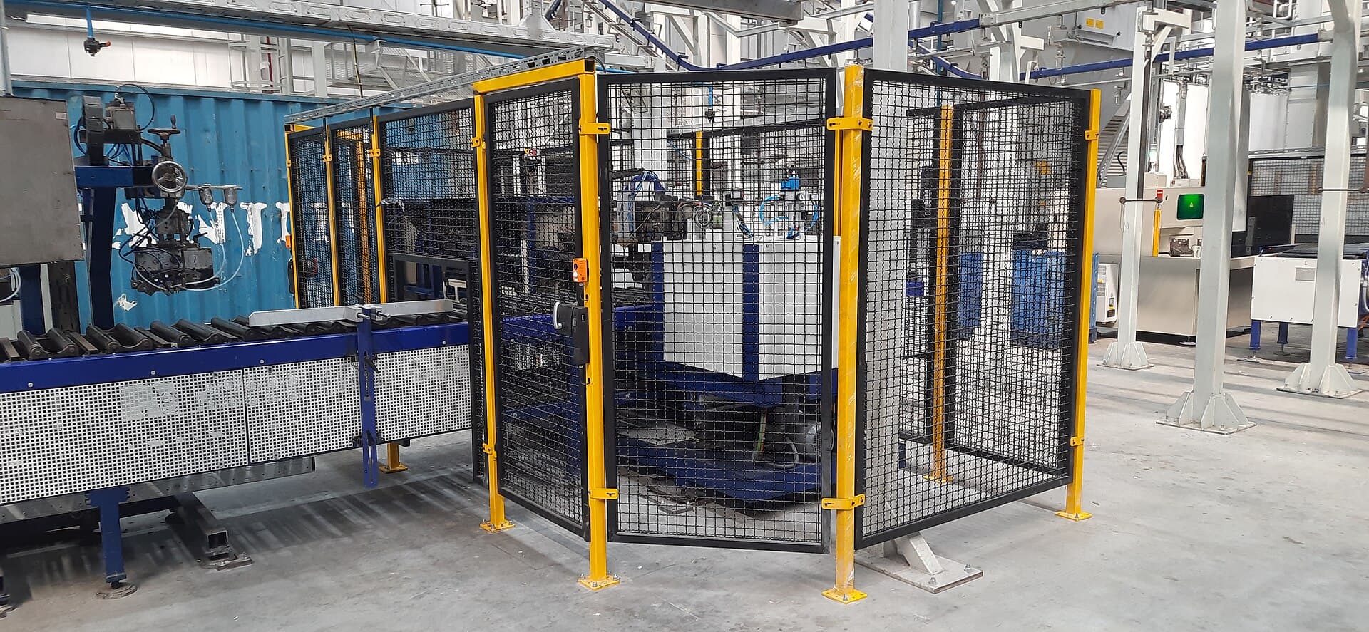Maskincell med gult skyddsstaket och transportband i en produktionshall